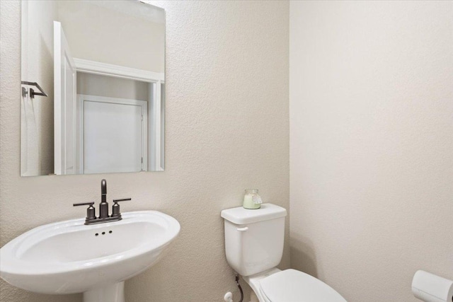 half bathroom featuring toilet, a sink, and a textured wall