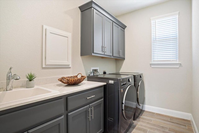 laundry area featuring cabinet space, baseboards, washing machine and clothes dryer, wood tiled floor, and a sink