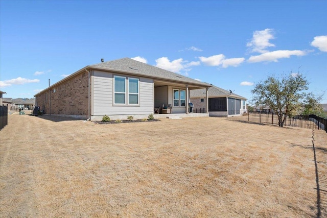 rear view of property with a sunroom, brick siding, and fence