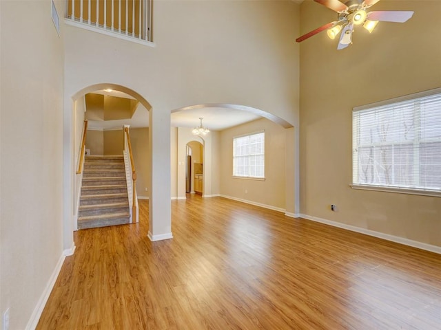 unfurnished living room with light wood-style floors, baseboards, arched walkways, and a ceiling fan