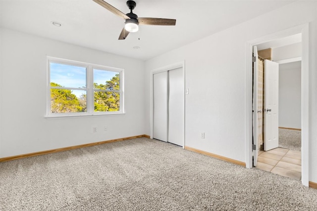 unfurnished bedroom featuring a closet, light colored carpet, light tile patterned flooring, ceiling fan, and baseboards