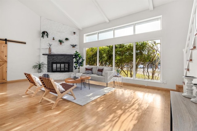 living room with a barn door, wood finished floors, beamed ceiling, a fireplace, and high vaulted ceiling