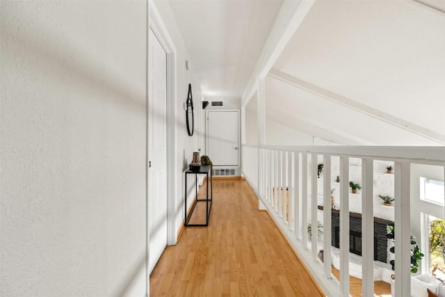 corridor featuring lofted ceiling with beams, a textured wall, light wood finished floors, and visible vents