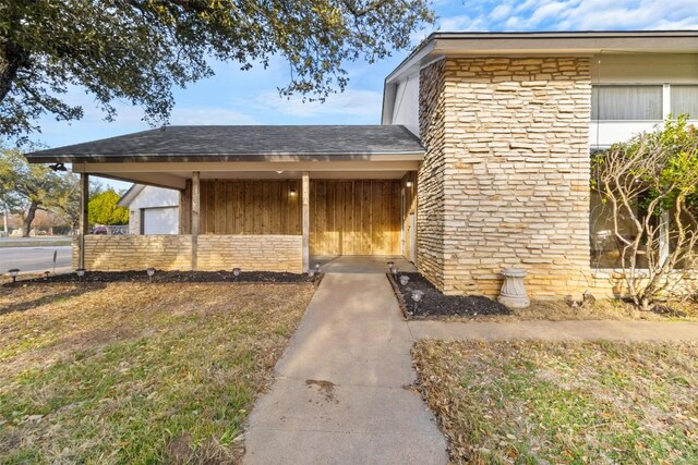 doorway to property featuring stone siding and roof with shingles