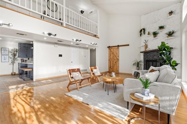 interior space featuring a stone fireplace, a barn door, wood finished floors, visible vents, and baseboards