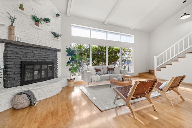 living room with beam ceiling, a stone fireplace, and wood finished floors