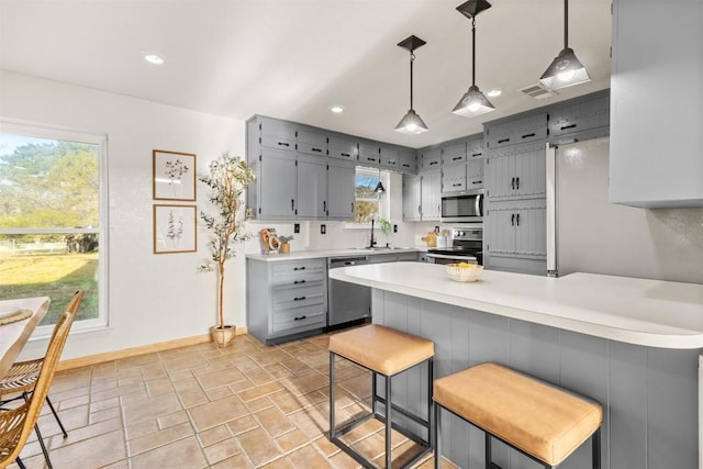 kitchen featuring a peninsula, a sink, light countertops, appliances with stainless steel finishes, and gray cabinets