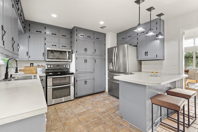 kitchen with stainless steel appliances, gray cabinets, a sink, and a peninsula