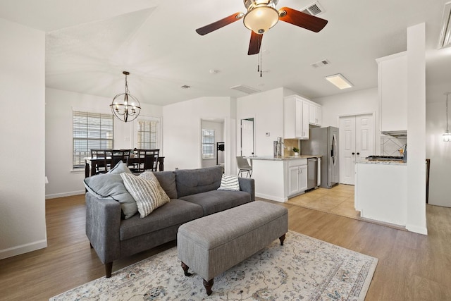 living room with light wood-type flooring, baseboards, visible vents, and ceiling fan with notable chandelier