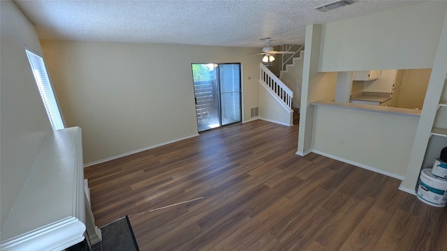 unfurnished living room featuring dark wood-style floors, visible vents, a textured ceiling, and stairs