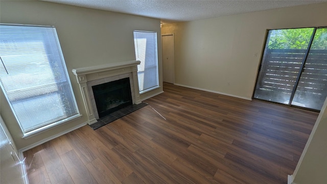 unfurnished living room with dark wood-style floors, a textured ceiling, a fireplace with flush hearth, and baseboards