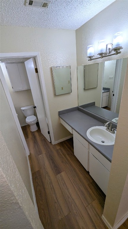 bathroom with a textured wall, toilet, wood finished floors, vanity, and visible vents