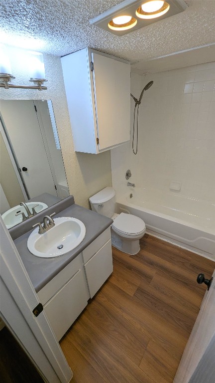 full bath with a textured ceiling, bathtub / shower combination, toilet, wood finished floors, and vanity