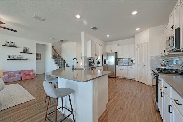 kitchen featuring visible vents, a breakfast bar area, open floor plan, stainless steel appliances, and a sink