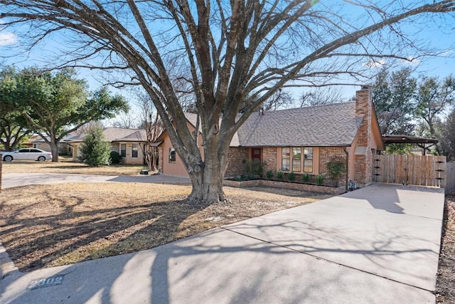 view of front of house with brick siding, roof with shingles, a chimney, concrete driveway, and fence