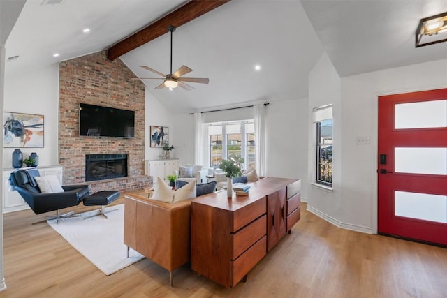 living room featuring ceiling fan, high vaulted ceiling, light wood-style flooring, a brick fireplace, and beamed ceiling