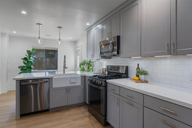 kitchen featuring stainless steel appliances, a peninsula, a sink, and gray cabinetry