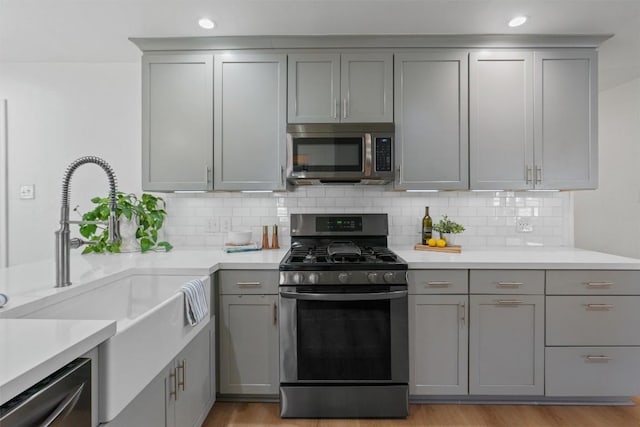 kitchen with appliances with stainless steel finishes, light wood-type flooring, a sink, and gray cabinetry