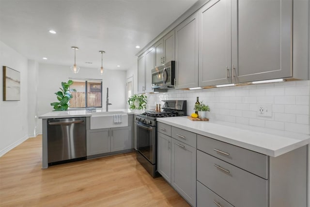 kitchen featuring a peninsula, appliances with stainless steel finishes, gray cabinets, and decorative backsplash