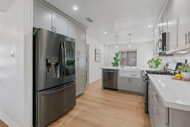 kitchen with stainless steel appliances, gray cabinets, light countertops, and a peninsula