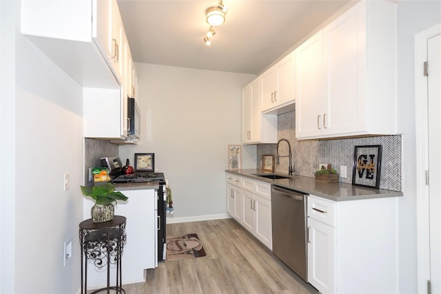 kitchen featuring light wood finished floors, a sink, stainless steel appliances, white cabinetry, and backsplash