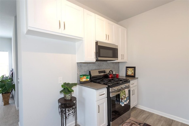 kitchen featuring light wood finished floors, baseboards, appliances with stainless steel finishes, white cabinetry, and backsplash