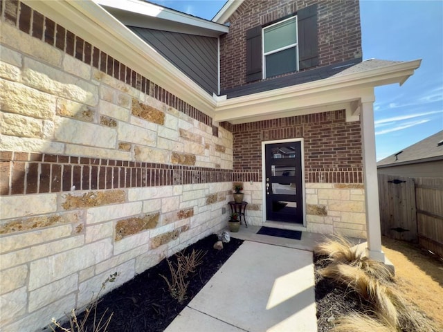 view of exterior entry featuring brick siding and fence