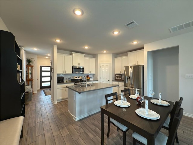 171 Longstraw Dr, Buda, TX 78610 - kitchen featuring stainless steel appliances, a sink, dark countertops, an island with sink, and white cabinetry