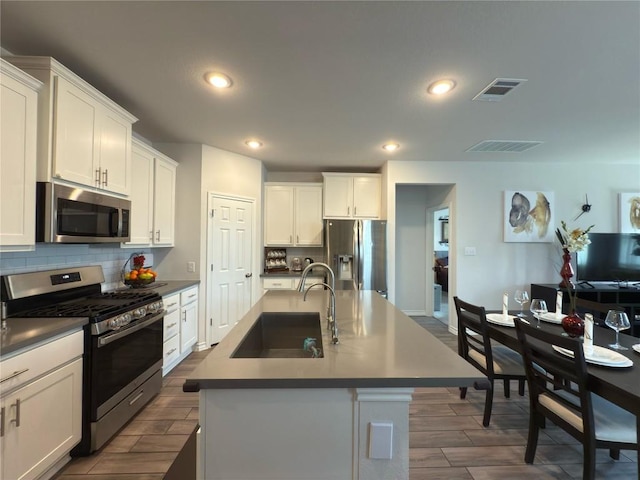 171 Longstraw Dr, Buda, TX 78610 - kitchen with appliances with stainless steel finishes, a sink, decorative backsplash, wood finish floors, and a center island with sink