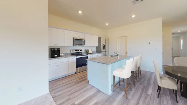 kitchen with a kitchen island with sink, stainless steel appliances, a sink, and white cabinetry