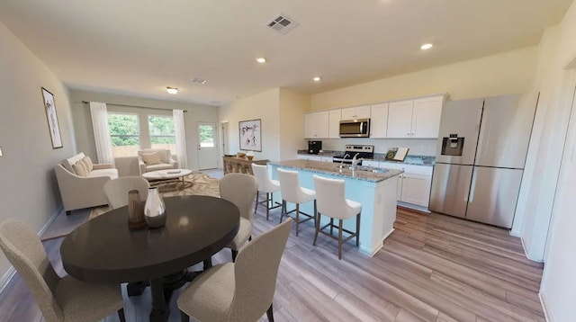 kitchen with a center island with sink, stainless steel appliances, visible vents, light wood-style flooring, and white cabinets