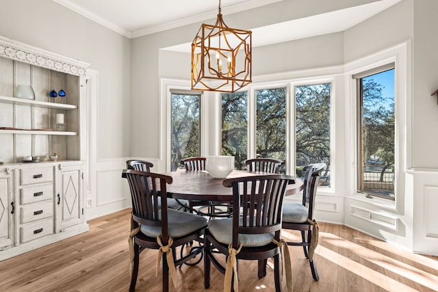 dining area featuring ornamental molding, light wood-type flooring, a notable chandelier, and a decorative wall