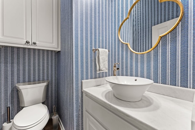 bathroom with toilet, vanity, and wallpapered walls