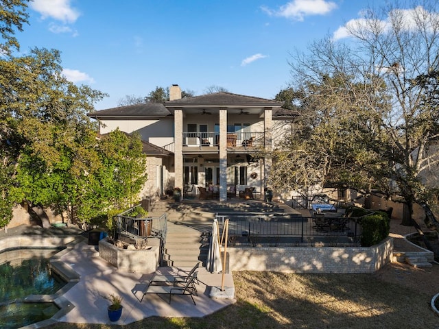 back of property with a patio, a balcony, a ceiling fan, stucco siding, and a chimney