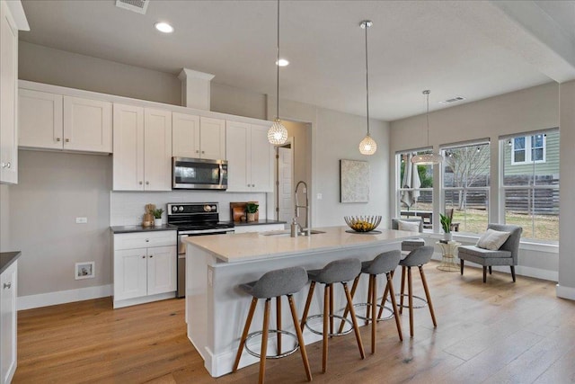 kitchen featuring light wood-style floors, decorative backsplash, stainless steel appliances, and a sink