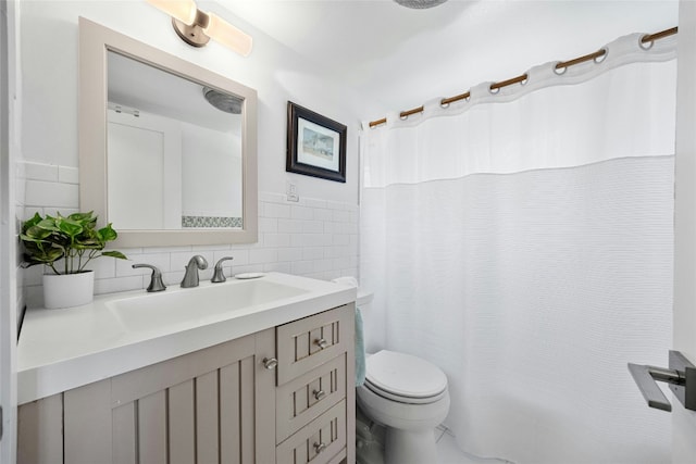 bathroom with wainscoting, toilet, a shower with curtain, vanity, and tile walls