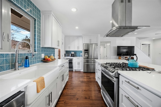 kitchen with stainless steel appliances, backsplash, white cabinets, a sink, and island range hood