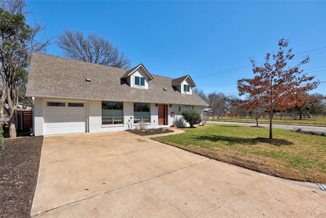 cape cod home featuring an attached garage, brick siding, concrete driveway, roof with shingles, and a front lawn