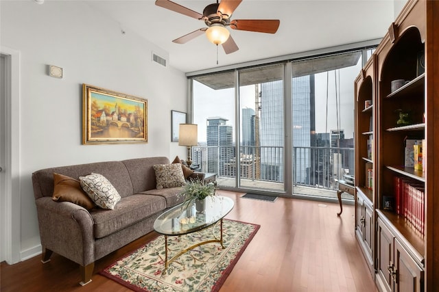 living room featuring visible vents, a ceiling fan, wood finished floors, a city view, and floor to ceiling windows