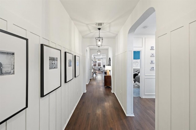 hall with dark wood-type flooring, arched walkways, visible vents, and a decorative wall