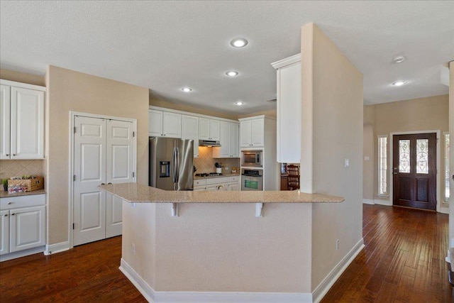 kitchen with a peninsula, dark wood-style floors, appliances with stainless steel finishes, and backsplash