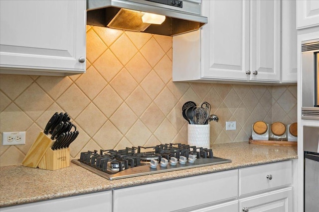 kitchen featuring under cabinet range hood, stainless steel gas cooktop, white cabinets, and decorative backsplash