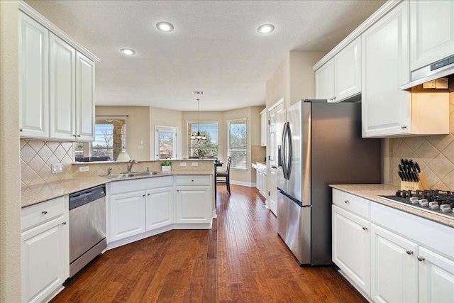 kitchen with dark wood finished floors, stainless steel appliances, white cabinetry, a sink, and a peninsula