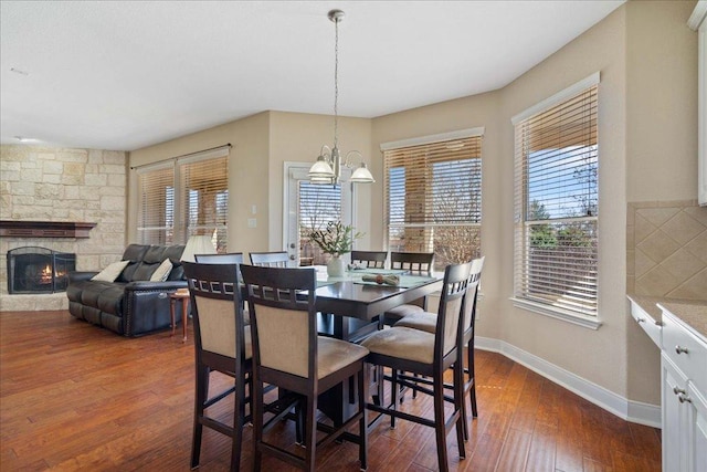 dining area featuring dark wood-type flooring, a notable chandelier, a fireplace, and baseboards