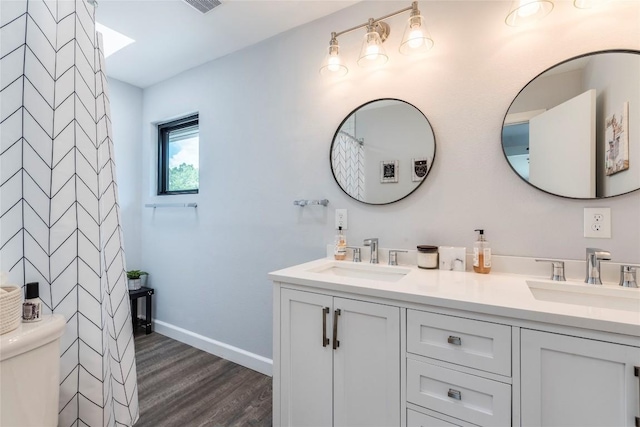 bathroom featuring wood finished floors, a sink, toilet, and double vanity