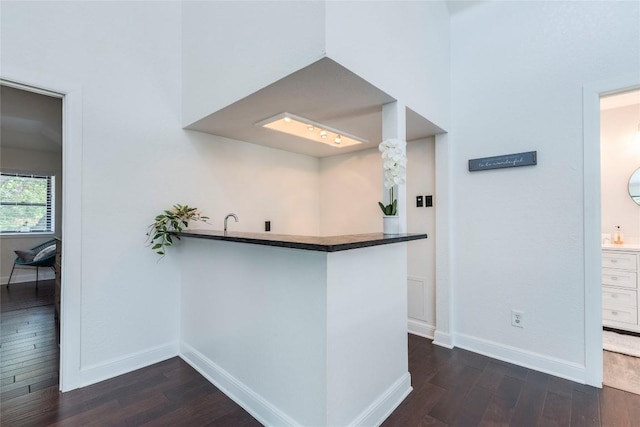 kitchen featuring dark wood-type flooring, dark countertops, a peninsula, and baseboards