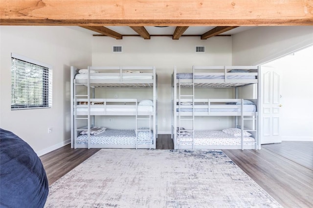 bedroom with beamed ceiling, wood finished floors, visible vents, and baseboards