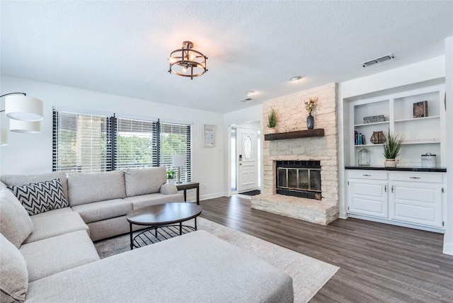 living room with dark wood-style floors, visible vents, a stone fireplace, a textured ceiling, and baseboards