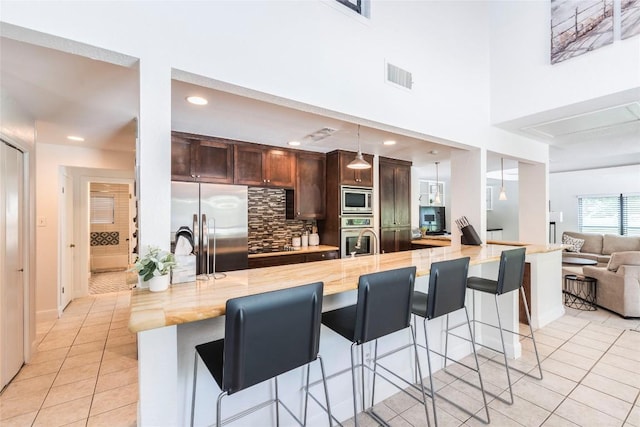 kitchen with light tile patterned floors, stainless steel appliances, a breakfast bar area, and visible vents