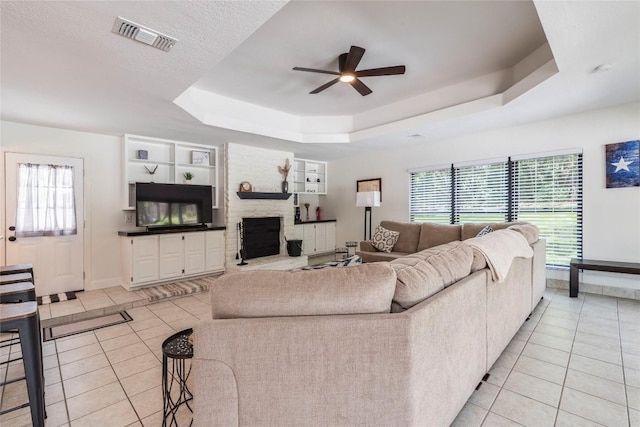 living room featuring a fireplace, a raised ceiling, visible vents, light tile patterned flooring, and ceiling fan